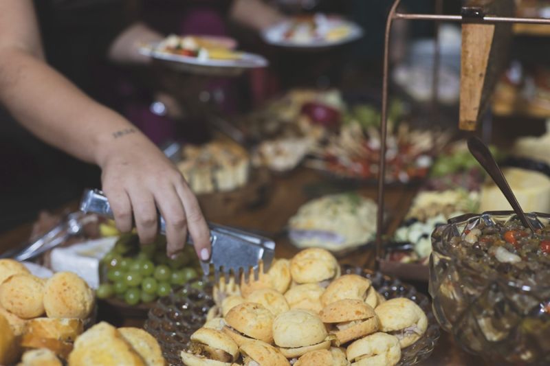 Convidado se servindo de uvas, com pão de queijo e quitutes na mesa