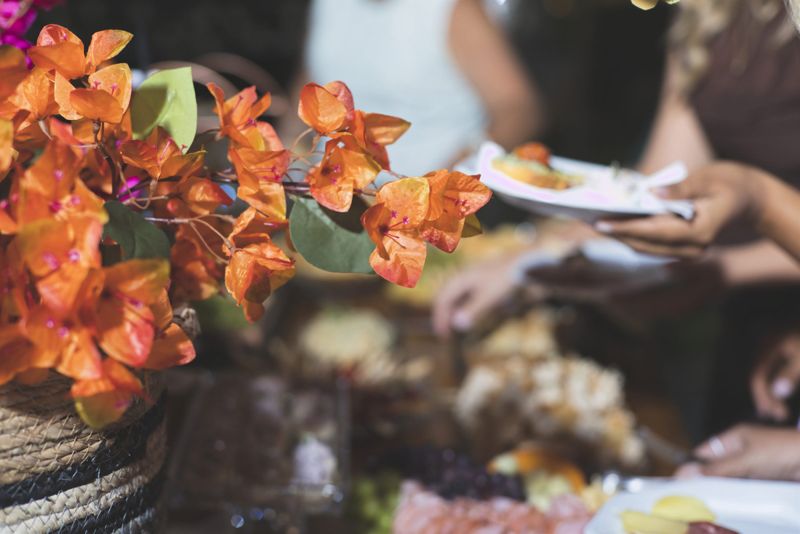 Convidados se servindo ao lado de flores laranjas